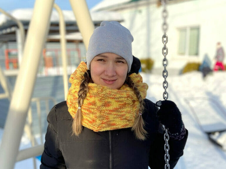 A woman in a yellow scarf standing on a swing.