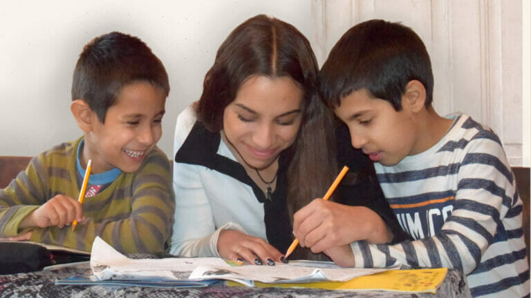 A group of children are sitting at a table with a teacher.