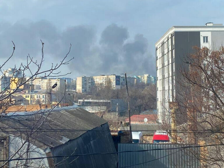 A black smoke billows from a building in a city.