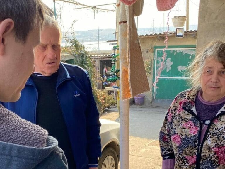 A woman is talking to an older man in front of a house.