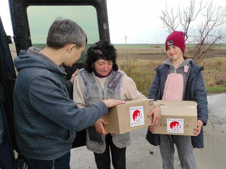 Three people standing in front of a van with boxes.