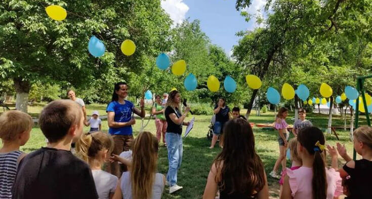 A group of children in a park with yellow and blue balloons.