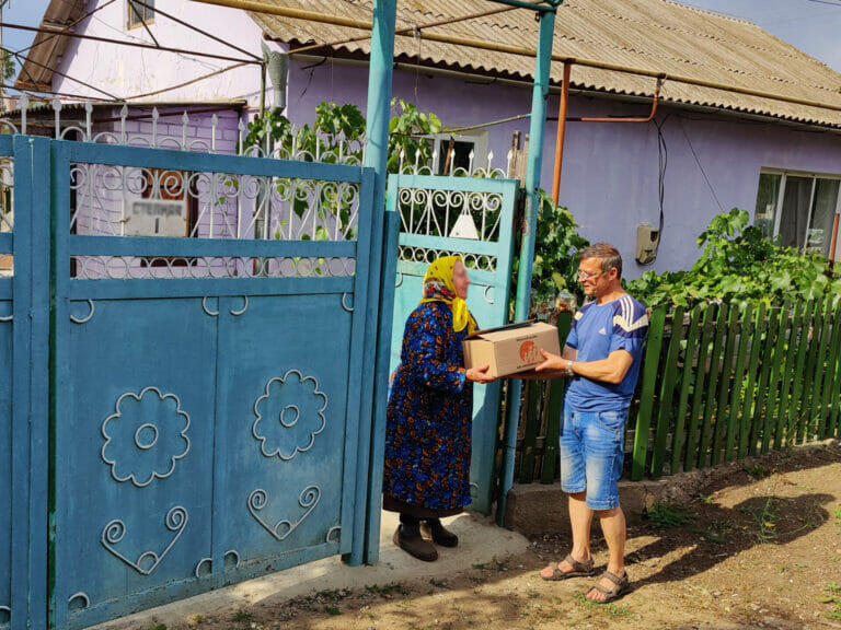 A woman delivering a box to a man at a blue gate.