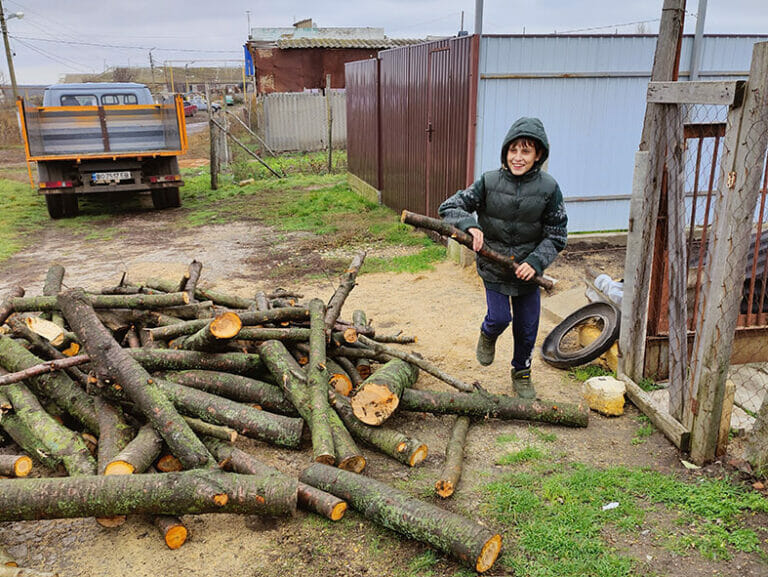 A boy is standing next to a pile of logs, ready for a Mission Possible.