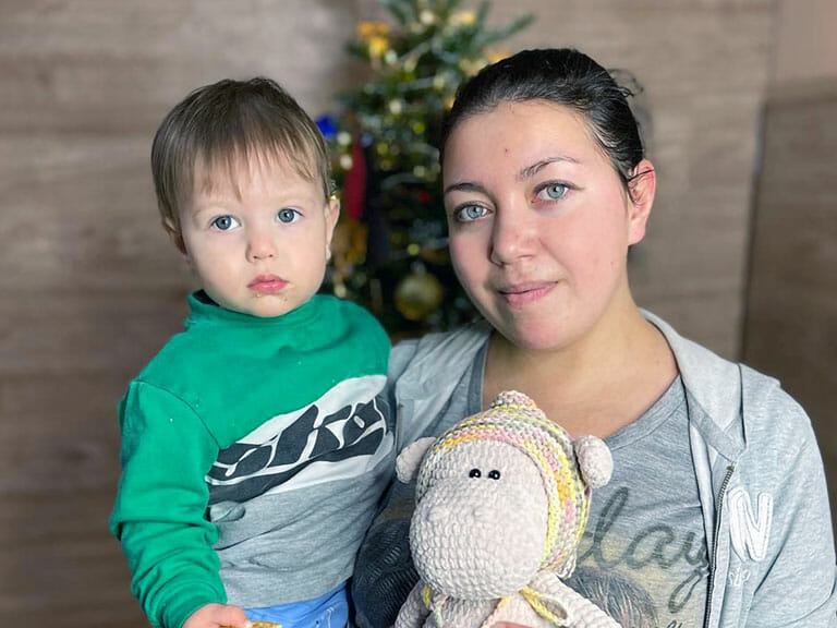 A woman holding a stuffed animal in front of a christmas tree for Mission Possible.