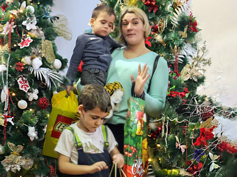 A woman and two children standing in front of a Christmas tree on a mission.