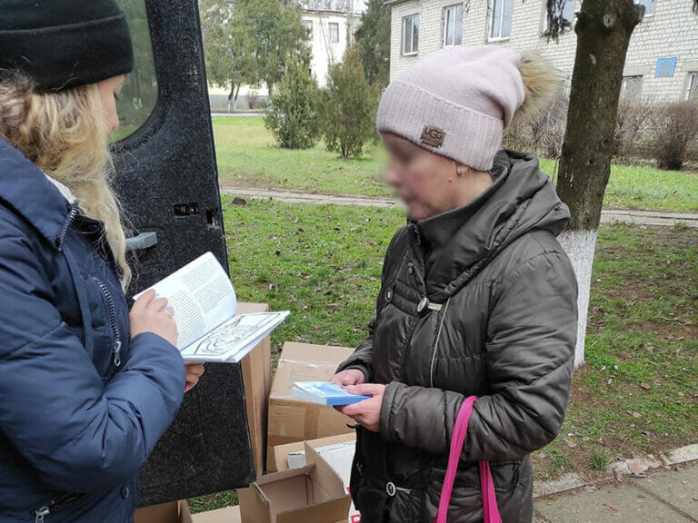 Two women on a mission standing next to a truck with a book in their hands.