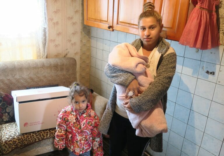 A woman holding a baby in a kitchen during Mission Possible.