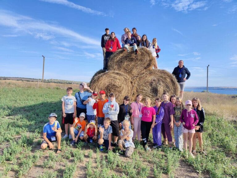 A group of people posing in front of a hay bale.