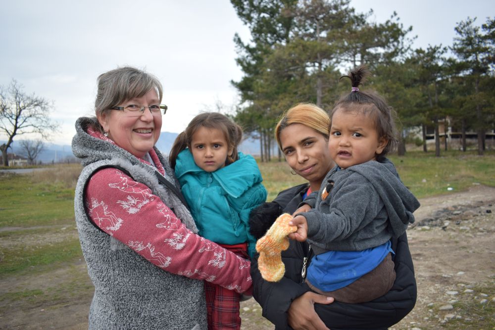 Two women standing outdoors, each holding a young child.